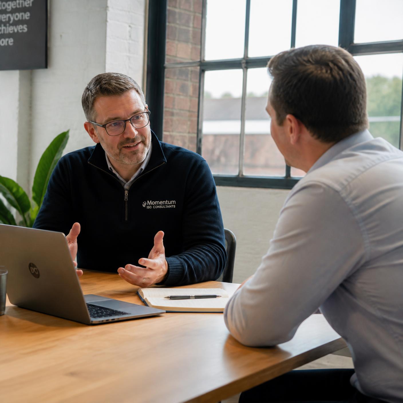 An ISO consultant and a client manager in a relaxed discussion across a table in a bright office