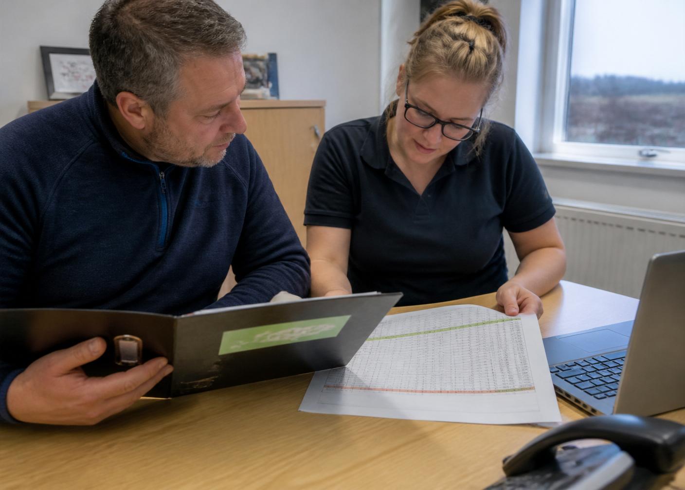 Two colleagues reviewing an environmental management system folder and compliance register in a UK office