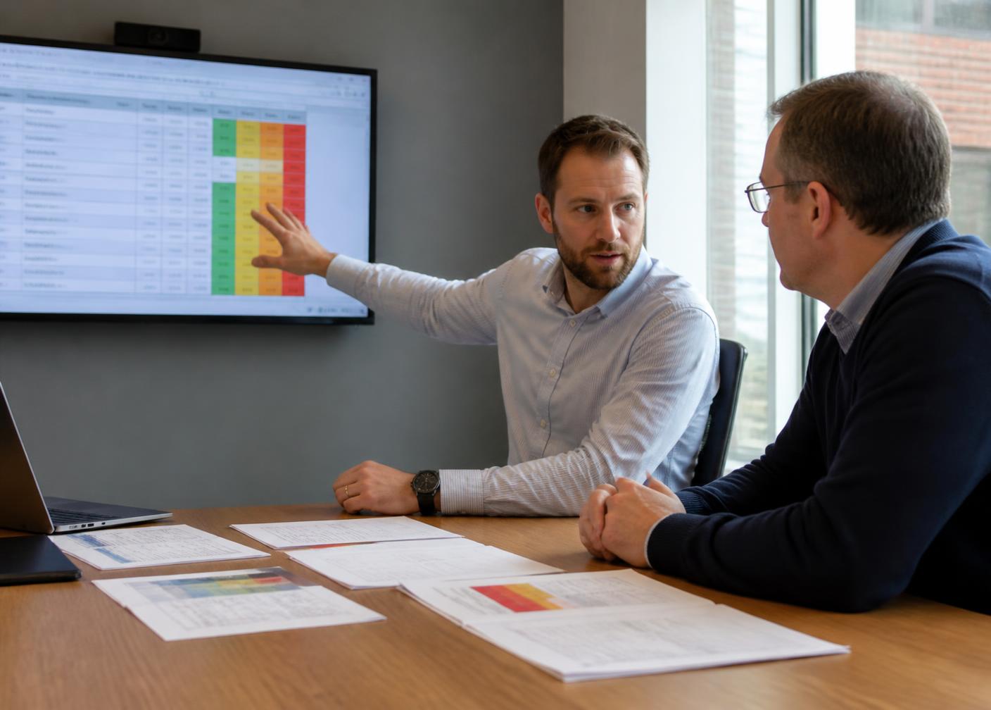 An ISO consultant walking an IT manager through an information security risk register in a UK meeting room