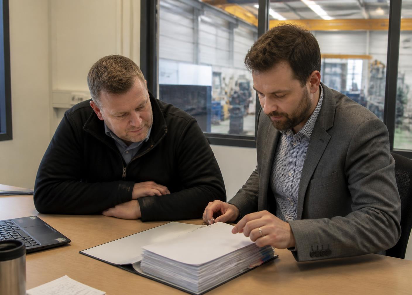 A consultant and an operations manager reviewing a single combined management system folder at a UK manufacturing site